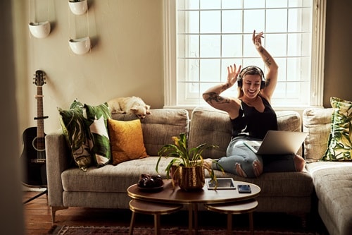 A woman is sitting on her couch listening to headphones